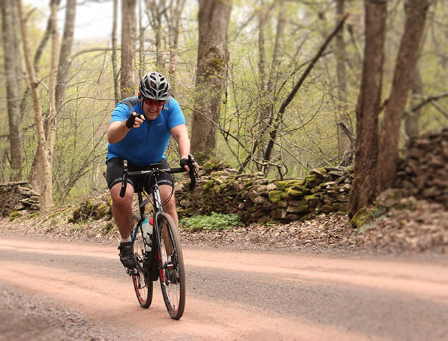 Rider cycling through woods, pointing with a large smile at the camera man